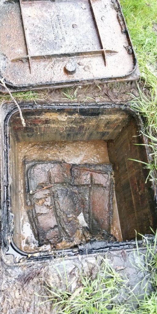 Open manhole full of debris and silt