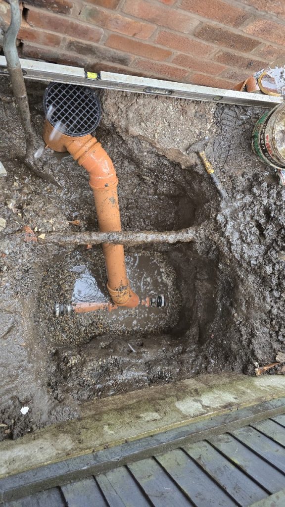 New gully and orange drainage pipe connection in an excavated trench