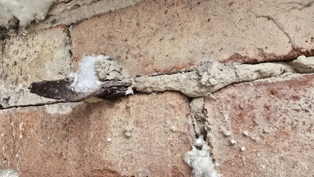 Rusted cavity wall tie exposed in cracked brickwork
